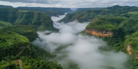 Sticker - Stunning aerial view of lush green valley shrouded in misty clouds, surrounded by majestic mountains and dense forest