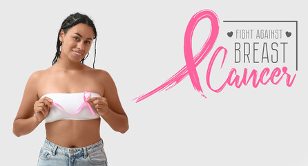 Wall Mural - Young African-American woman with pink ribbon on white background. Breast cancer awareness concept