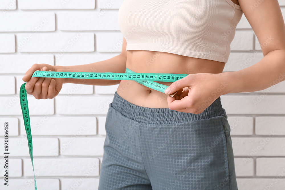 Young woman with measuring tape on light background. Diet concept