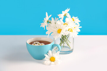 Wall Mural - Cup of natural chamomile tea and flowers on white table near blue wall