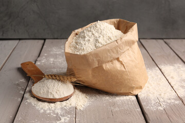 Canvas Print - Paper bag with flour, wooden spoon and wheat ear on grey wooden table near wall