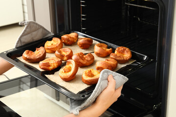 Wall Mural - Woman taking baking tray with tasty Yorkshire pudding out from oven in kitchen