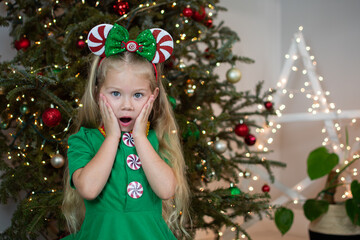 Portrait of a cute Caucasian little girl in an Elf costume being surprised near the Christmas tree. Kids and Christmas concept