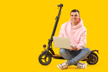 Sticker - Young man with electric scooter using laptop on yellow background