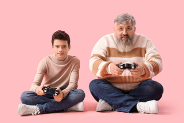 Poster - Happy grandfather with his cute grandson playing video games on pink background