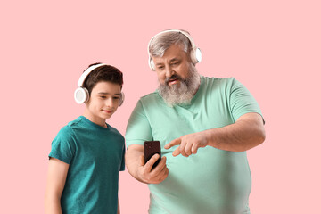 Wall Mural - Happy grandfather and his cute grandson in headphones with mobile phone on pink background