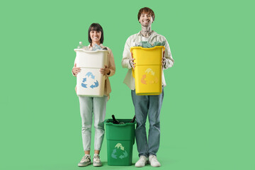 Wall Mural - Young couple with containers for garbage on green background. Recycling concept