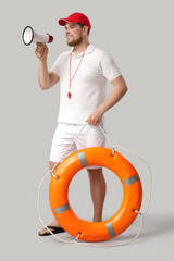 Wall Mural - Young male lifeguard with ring buoy and megaphone on grey background