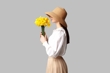 Wall Mural - Beautiful young woman with bouquet of beautiful narcissus flowers on grey background