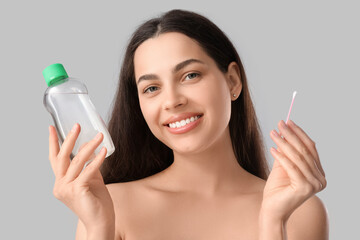 Sticker - Beautiful young happy woman with cotton bud and bottle of micellar water on grey background