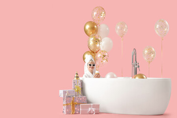 Sticker - Happy young woman in bathtub with birthday cupcake, gift boxes and balloons on pink background