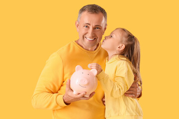 Poster - Little girl with her father holding piggy bank on yellow background