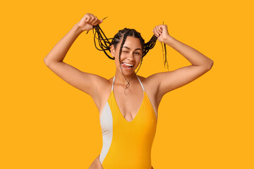 Sticker - Beautiful young African-American woman in stylish swimsuit showing tongue on yellow background