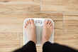 © sofiko14 - Person standing on scale measuring weight on wooden floor. Health and fitness concept focusing on weight management and wellness.