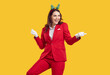 © Studio Romantic - New Year's mood and fun. Beautiful stylish woman dancing having fun new year occasion on orange background in studio. Girl in red suit, white gloves and decorative New Year's hoop on head is smiling.