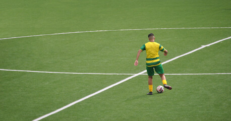 Football player in the midfield area preparing a passing movement with yellow and green equipment, synthetic green