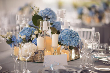 banquet table is decorated with plates, cutlery, glasses, candles and flower arrangements. blue and white flowers decorate the table. 