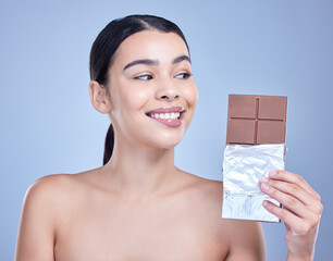 Skincare, smile and woman with chocolate bar and sweets in studio isolated on blue background. Makeup, beauty and model eating cocoa candy for diet, cosmetics and unhealthy sugar food for diabetes