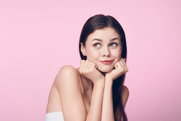 Wall Mural - Beautiful young woman posing with her hands on her chin on a pink background