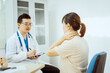 © Phushutter - A male Asian pediatrician in a white lab coat sits at his desk, warmly greeting a middle-aged pregnant woman for a prenatal consultation, offering care and support in a clinical setting.