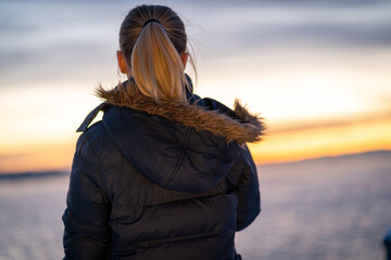 blond girl watching the sunset over akker brygge in oslo norway on a cold winter day