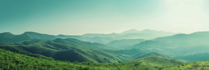 A scenic view of green hills stretching towards distant mountains under a misty sky, creating a tranquil and refreshing landscape.