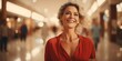 © Kakabe - A woman with blonde hair and a red blouse smiles joyfully in a modern, softly lit shopping mall perfect for ads emphasizing happiness, retail therapy, or lifestyle themes,