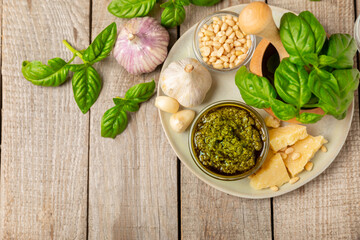 Pesto. Italian basil pesto sauce on a textured wooden background. Ingredient for pesto sauce: fresh basil, pine nuts, Parmesan cheese and olive oil. Space for text.Copy space.