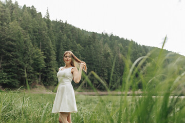 A woman with long red hair is standing in a field of tall grass