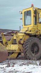 Poster - Yellow tractor at the construction site. Clip. Cold winter ground and wooden boards on a cloudy sky background.