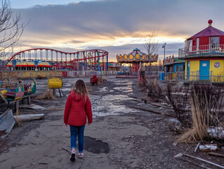 Wall Mural - A girl walks through a deserted amusement park. The park is in a state of disrepair, with broken rides and a desolate atmosphere. The girl appears to be alone