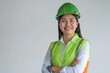 © ChaoticMind - A smiling woman in a green helmet and reflective safety vest stands with crossed arms, showcasing confidence and positivity on a construction or industrial site.