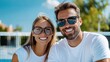 © Pinklife - A cheerful couple in sunglasses posing happily at a tennis court during a sunny day, both dressed in white attire, enjoying the outdoor environment together.