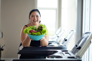 Portrait fat woman enjoying eating vegetable salad. beautiful young chubby overweight woman wearing sporty fitness clothes doing exercise indoors at gym fitness sport club, body and health care