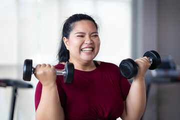 Young woman exercising with dumbbells. beautiful young chubby overweight woman wearing sporty fitness clothes doing exercise indoors at gym fitness sport club, body and health care