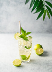 Mojito cocktail in a tall glass with lime, mint and ice on a light background. Trendy summer refreshing lemonade drink concept