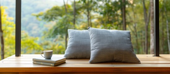 wooden terrace with large windows overlooking the forest, two grey pillows and books on it