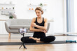 © sofiko14 - Woman doing yoga stretching exercise during online class at home. Female fitness instructor filming workout routine on smartphone. Healthy lifestyle and self-care in cozy living room.