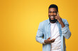 © Prostock-studio - Cheerful african american man talking on phone and laughing out loud over yellow studio background, free space