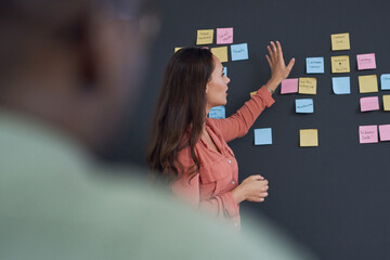 Woman, coach and blackboard with sticky notes in office for training, teaching and learning for skill development. People, employee and mentor or leader at workshop with internship program for career