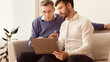 © Prostock-studio - Mature man teaching old dad to use laptop, computer programs and browse internet sitting on sofa indoor. Panorama