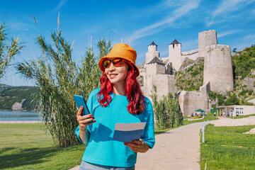 Wall Mural - A woman uses her smartphone to navigate towards Golubac Fortress in Serbia, checking her map for the best route to explore architecture and historical landmarks along the Danube River.