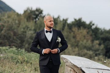 A man in a black suit and white tie is standing in a field. He is wearing a white flower in his lapel. Concept of elegance and sophistication, as the man is dressed in formal attire