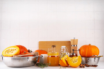 Wall Mural - Pumpkins cooking background with sliced and whole pumpkin halves or butternut squash, raw herbs. spices on white background with cutting board, herbs, honey. Thanksgiving dinner seasonal cooking