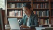 © WS Studio 1985 - Focused on Research:  A young woman in a blazer intently types on her laptop in a library, surrounded by towering bookshelves, evoking a sense of intellectual pursuit and scholarly concentration.