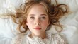 © Feuerbach - A young girl with blonde hair and freckles, lying on a white background, wearing a lace dress.