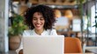 © Pinklife - A cheerful woman with curly hair works on her laptop in a cozy coffee shop, surrounded by warm lighting and greenery, exuding a positive and productive atmosphere.