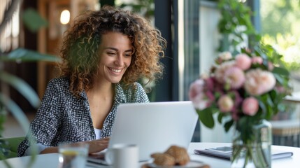 A woman sits in a trendy cafe, working on her laptop with a smile on her face, set against a background of flowers and natural light streaming through the window.