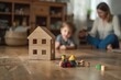 © Muneer - Wooden house model on the floor, a family playing with toys in a blurred living room background.
