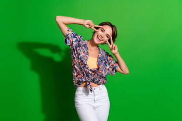 Sticker - Photo of adorable lovely woman with bob hairstyle dressed print blouse showing v-sign on face isolated on vivid green color background